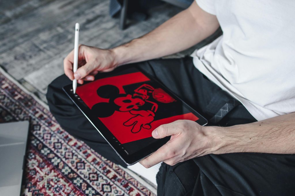 A person sitting indoors drawing a cartoon character on a tablet using a stylus.